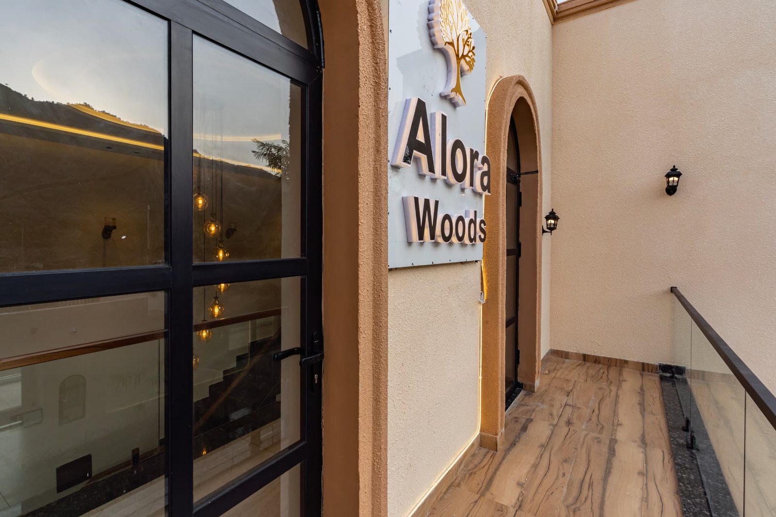 Alora Woods signage at the villa entrance with glass doors and warm lighting